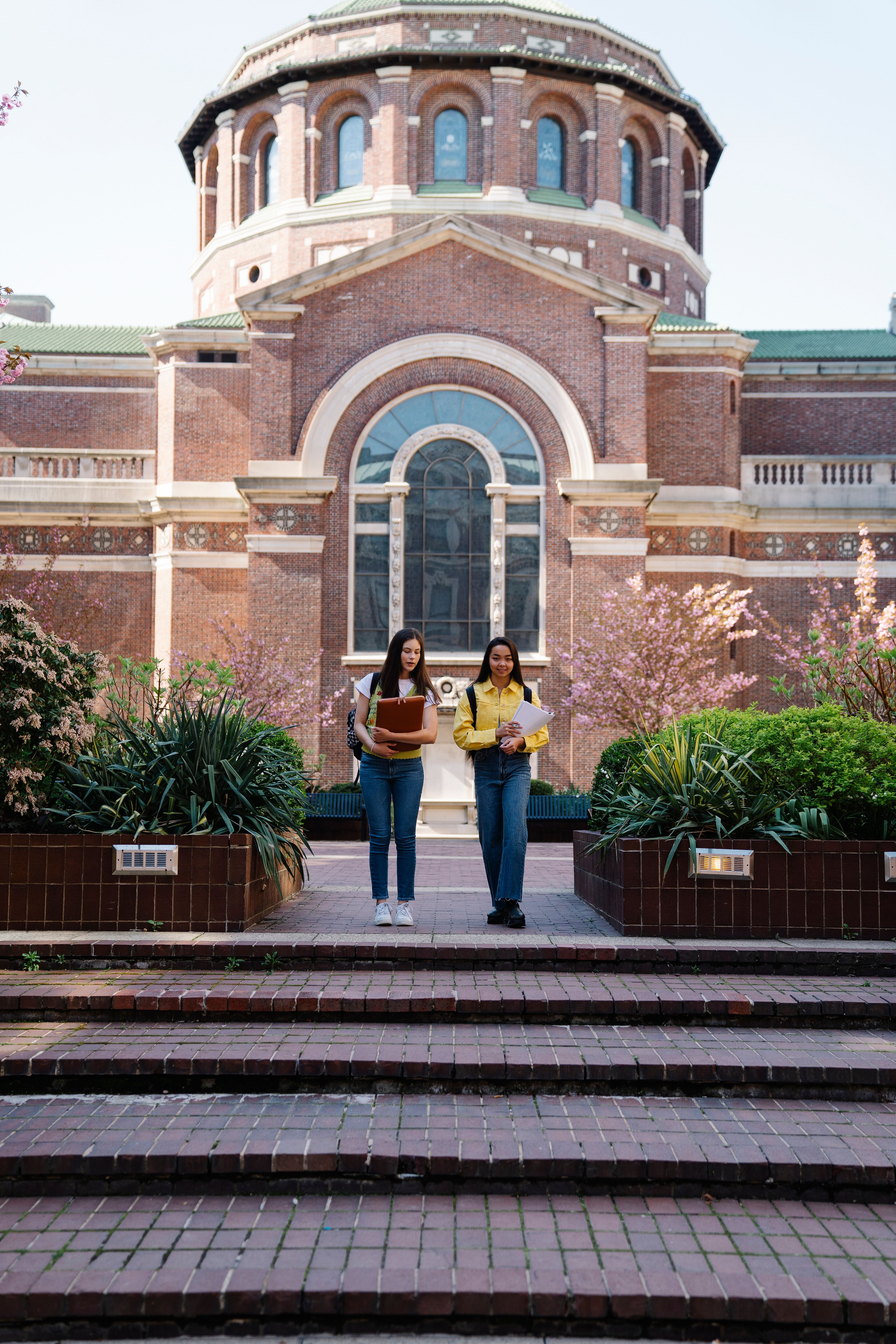 Two young women walking past a historic university building on a sunny day
