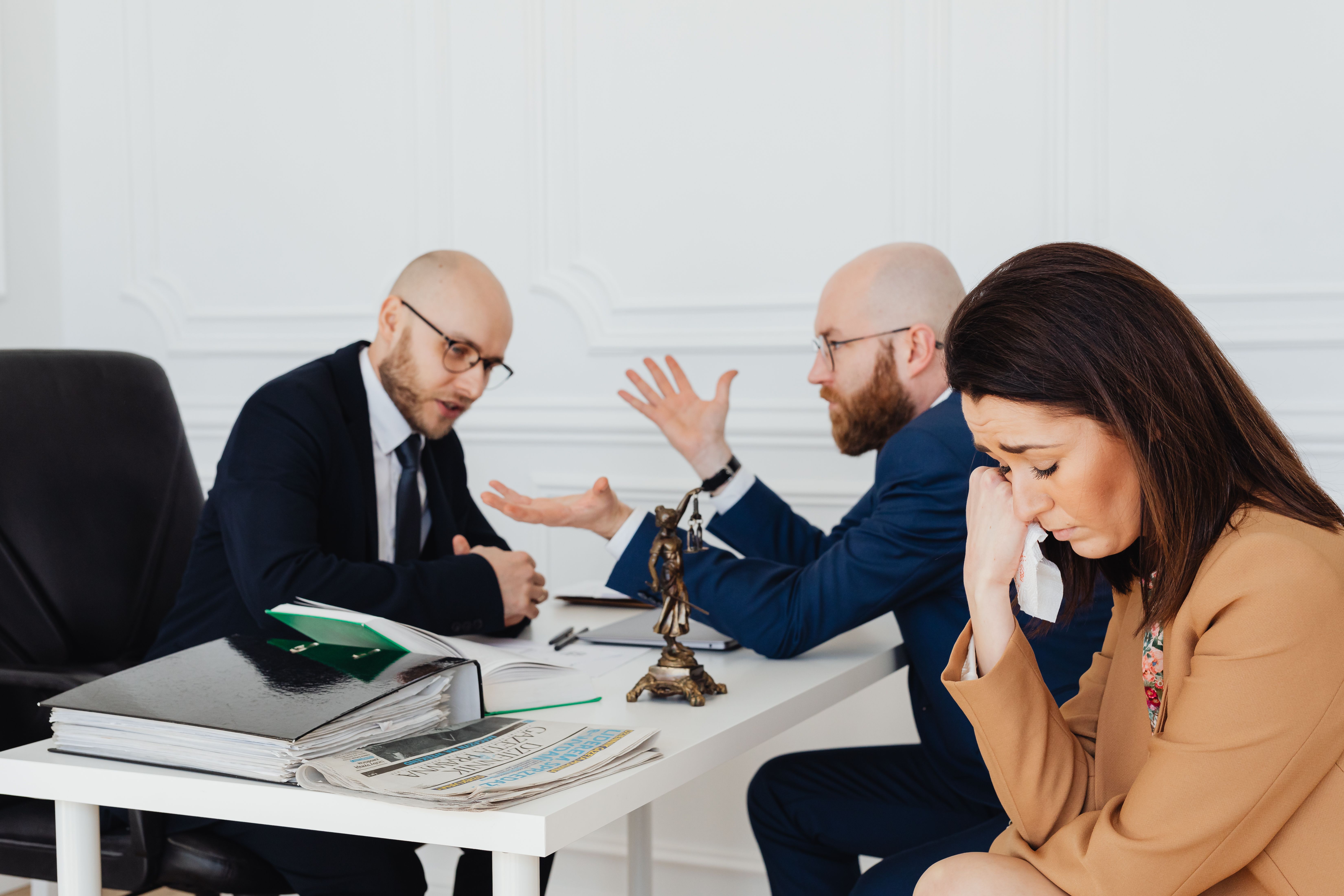 Distressed woman speaking with two lawyers in an office about a consumer class action claim