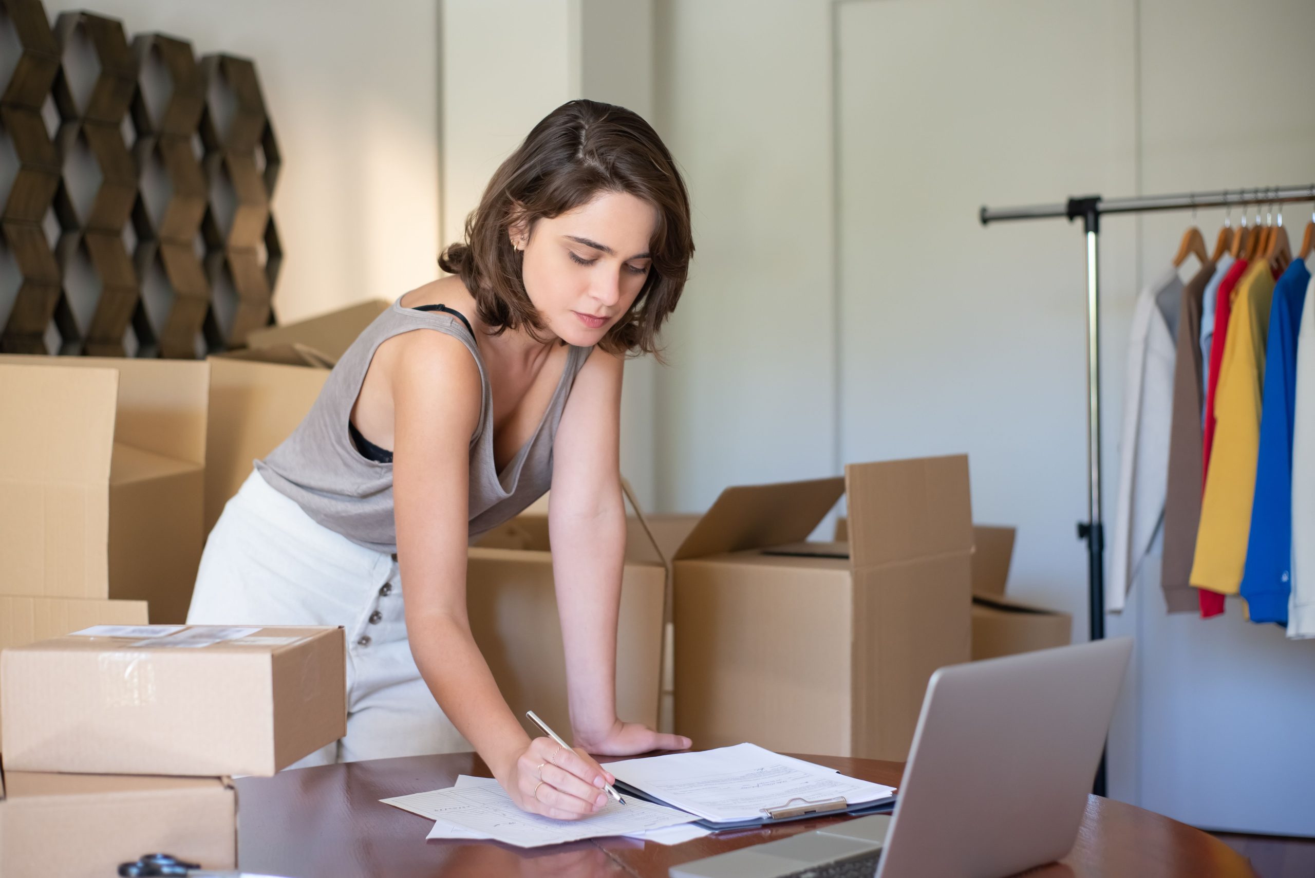 Small business owner managing her online shop from a home office with laptop and shipping boxes