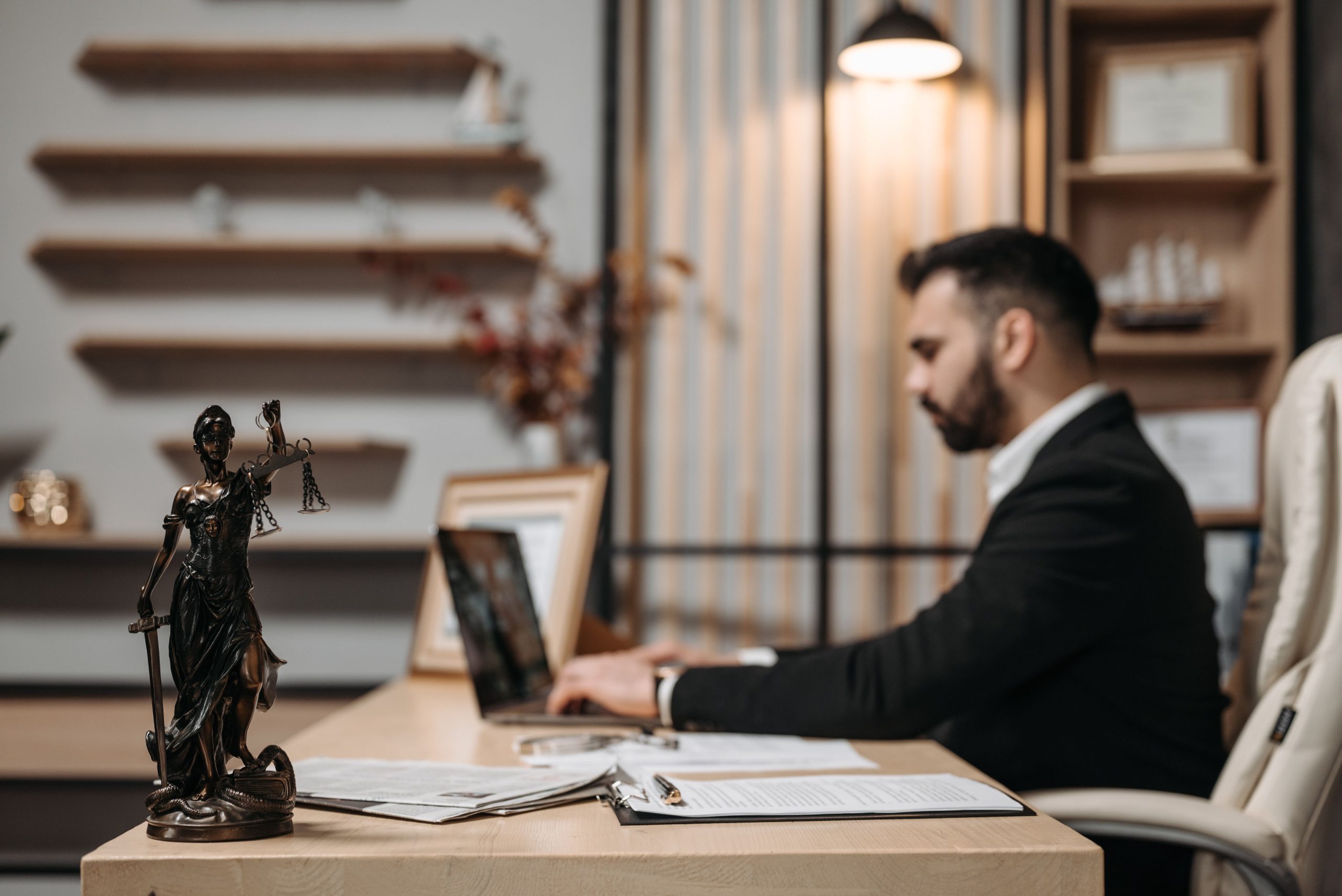 Lawyer working on a laptop in a modern law office beside a Lady Justice statue